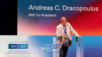 Andreas Dracopoulos, President of the Stavros Niarchos Foundation, speaks at the podium and behind him is a banner that reads Andreas C. Dracopoulos, SNF Co-President and below him is the logo of the Stavros Niarchos Foundation and the iMEdD logo.